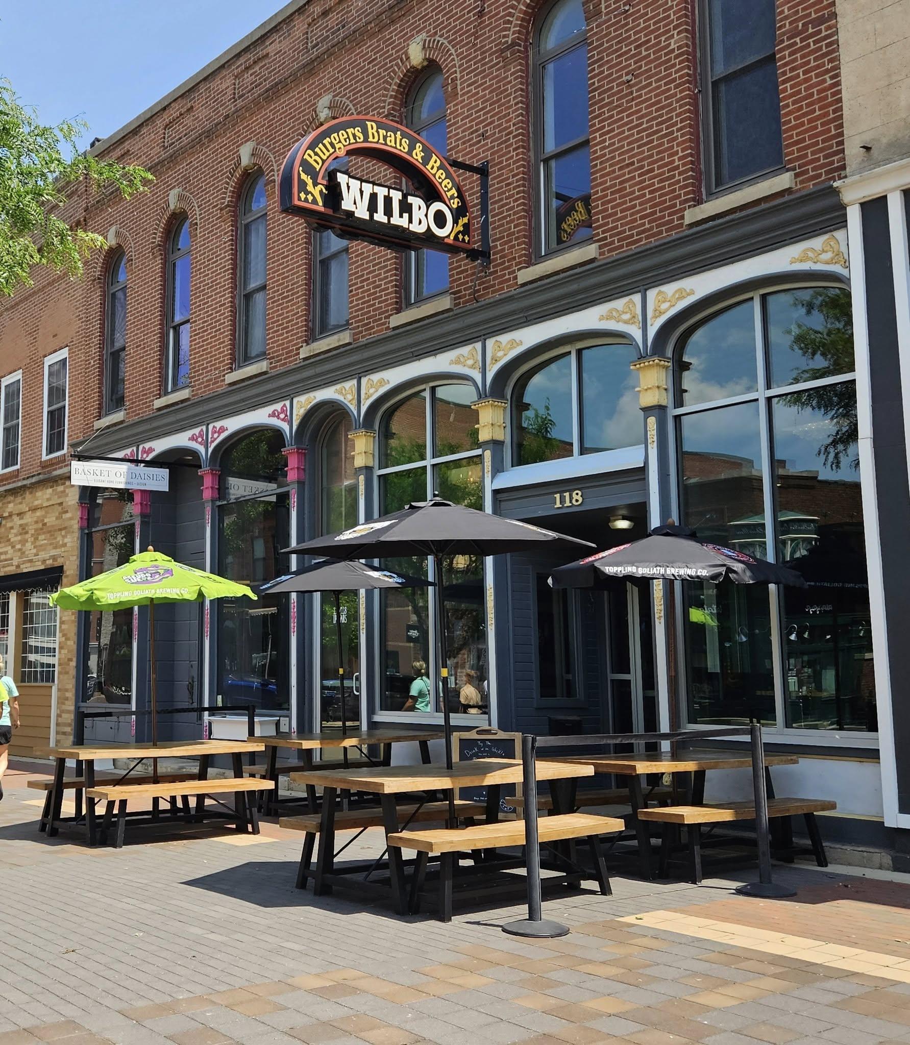 The Wilbo Burgers Brats and Beers storefront on Main Street in downtown Cedar Falls, with outdoor seating under Toppling Goliath Brewing umbrellas